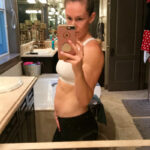 fit pregnant mom in a white sports bra taking a picture of her 13 week baby bump