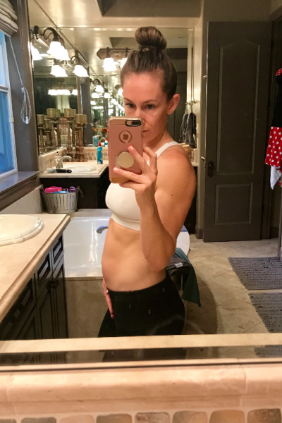fit pregnant mom in a white sports bra taking a picture of her 13 week baby bump