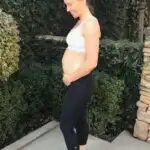 fit mom pregnant in a sports bra posing holding her hands under her baby bump