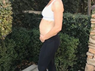 fit mom pregnant in a sports bra posing holding her hands under her baby bump