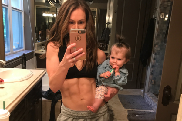 fit mom with a flat stomach standing in the mirror with her baby