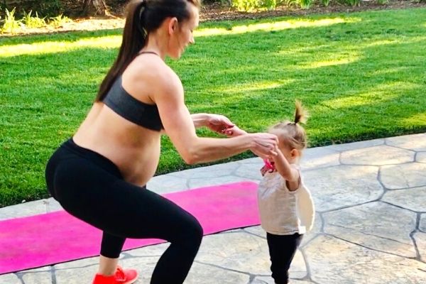 fit pregnant mom squatting with her baby