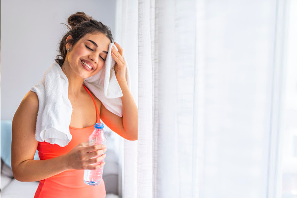 fit women wiping the sweat off her forehead holding a water bottle 