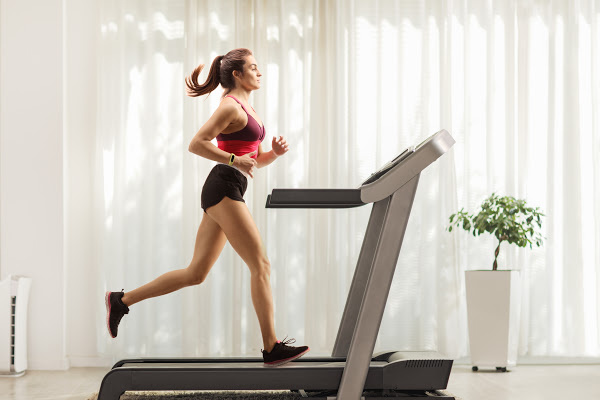 Full length profile shot of a young woman running on a treadmill at home