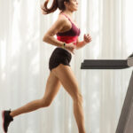 Full length profile shot of a young woman running on a treadmill at home