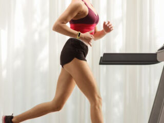 Full length profile shot of a young woman running on a treadmill at home