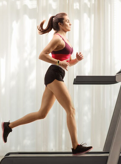 Full length profile shot of a young woman running on a treadmill at home