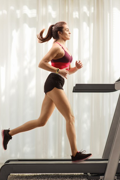 Full length profile shot of a young woman running on a treadmill at home