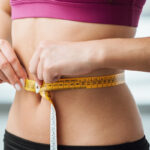 Slim young woman measuring her thin waist with a tape measure, close up