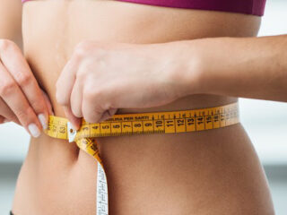 Slim young woman measuring her thin waist with a tape measure, close up