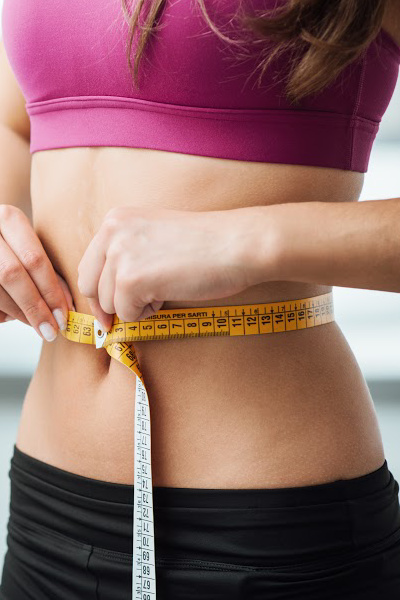 Slim young woman measuring her thin waist with a tape measure, close up