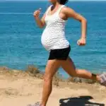 fit mom running during pregnancy in black shorts and a white top looking over the ocean