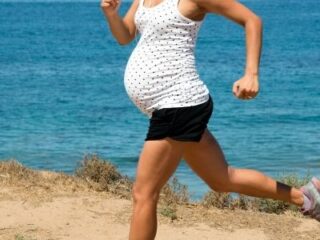 fit mom running during pregnancy in black shorts and a white top looking over the ocean
