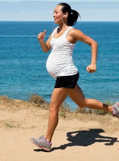 fit mom running during pregnancy in black shorts and a white top looking over the ocean