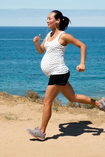 fit mom running during pregnancy in black shorts and a white top looking over the ocean