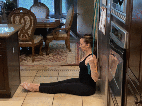 fit pregnant mom sitting with her back against a wall doing a lat pull down exercise for neck pain during pregnancy