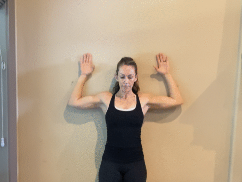 mom wearing all black standing against a wall doing wall angels to relieve neck pain in pregnancy