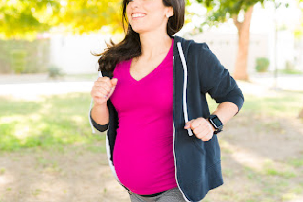 Active pregnant woman in her 30s smiling while walking in the park to stay healthy and fit during her pregnancy