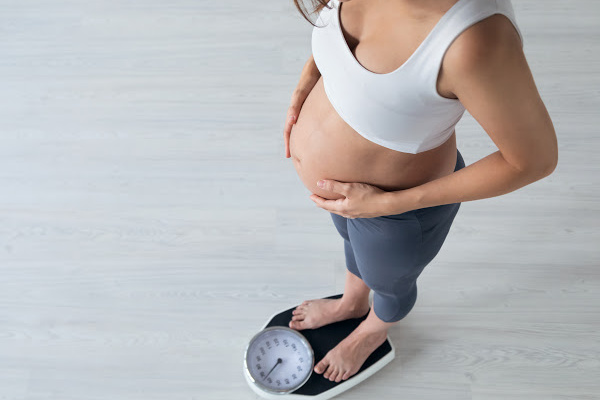 pregnant women in a white sports bra and black pants standing on a scale