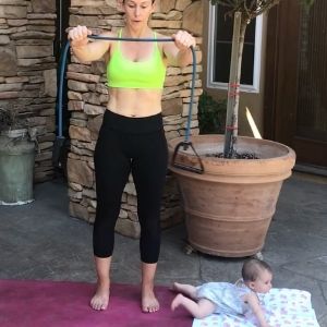 pregnant mom in black pants and green sports bra exercising with a baby on her pink yoga mat