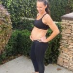 Fit pregnant mom in black pants and black sports bra holding her pregnant belly in the second trimester