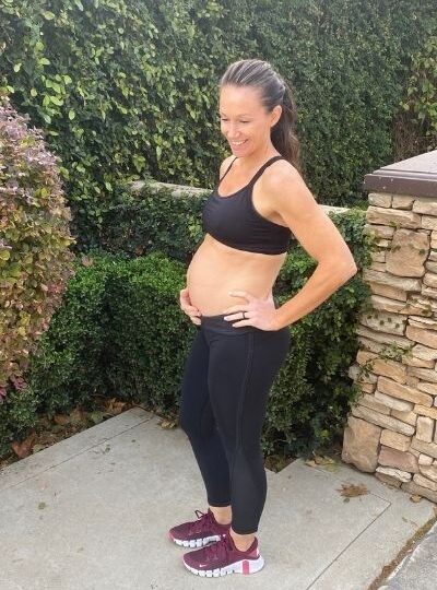 Fit pregnant mom in black pants and black sports bra holding her pregnant belly in the second trimester