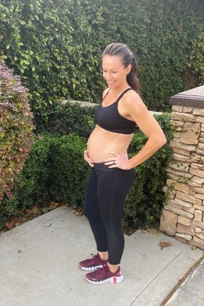 Fit pregnant mom in black pants and black sports bra holding her pregnant belly in the second trimester