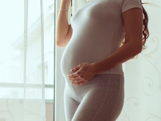 pregnancy mom standing in front of the window with hand on her belly, drinking coffee