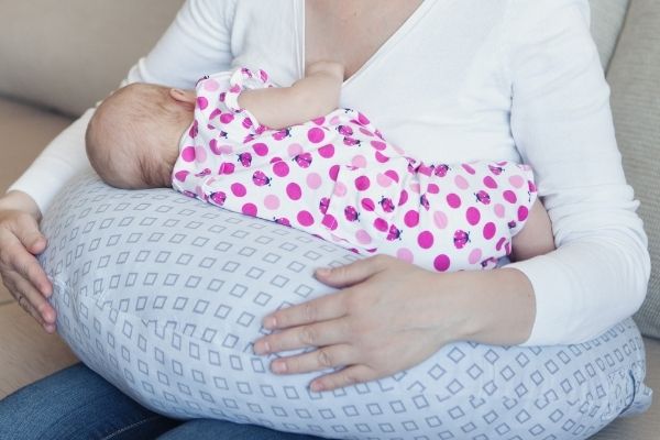 mom breastfeeding her baby with the help of a breastfeeding pillow. She is sitting with good posture while her baby breastfeeds