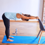 pregnant female on a blue yoga bent over and holding the back of a chair to stretch her back