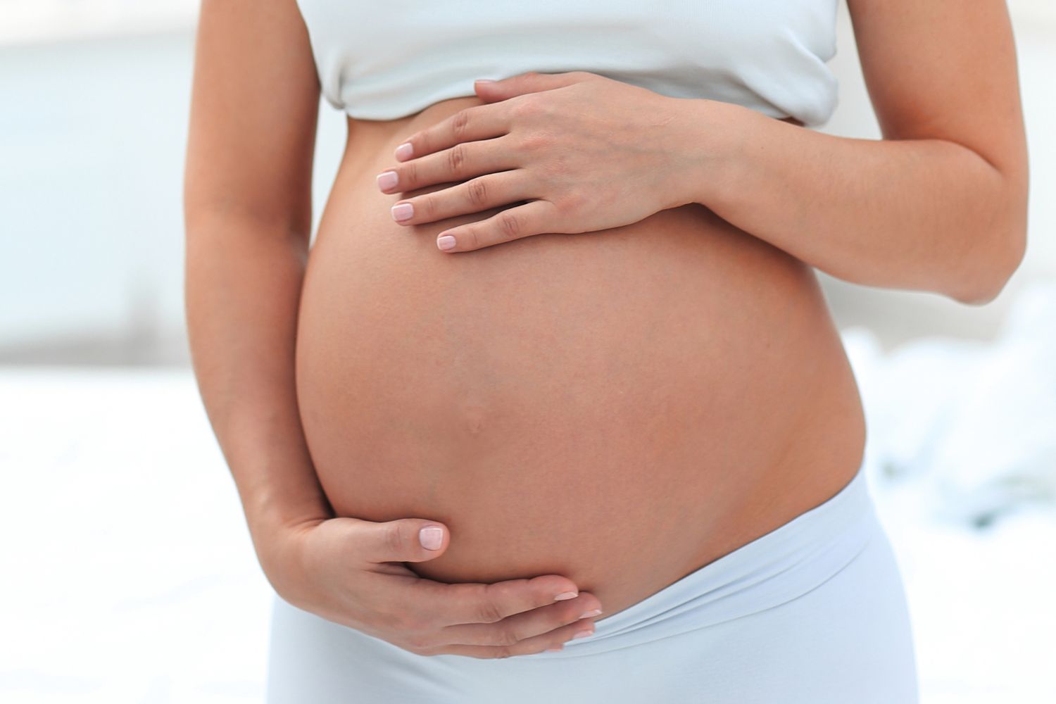 portrate of a young pregnant women on a light background holding her pregnant belly with her hands