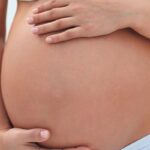 young pregnant mom in light clothes holding her belly with both hands