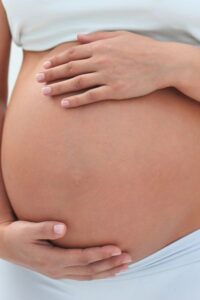 young pregnant mom in light clothes holding her belly with both hands